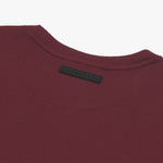 Close-up of the back neckline of a maroon T-shirt featuring a black rectangular label with embossed text that reads 'James Bark.' The T-shirt has a ribbed texture and is displayed against a plain white background." Let me know if you'd like any edits