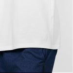 Close-up of the lower hem of the plain white T-shirt, showing the stitching detail over blue pants