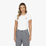 Front waist-up view of a female model wearing a white crew neck t-shirt with a small gold embroidered logo on the left chest, paired with grey trousers