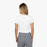 Back waist-up view of a female model wearing a plain white short-sleeve crew neck t-shirt tucked into grey trousers
