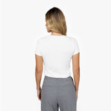 Back waist-up view of a female model wearing a plain white short-sleeve crew neck t-shirt tucked into grey trousers