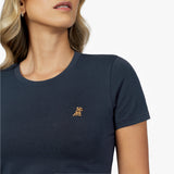 Close-up detail of the navy blue crew neck t-shirt worn by a model, showing the fabric texture and the small gold embroidered dog logo on the left chest