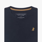 Close-up of the neckline of a navy blue crew neck James Bark t-shirt, showing the brand label, contrast neck tape, and gold embroidered dog logo on the chest