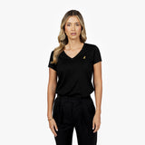Front waist-up view of a female model wearing a black v-neck t-shirt with a small gold embroidered logo on the left chest, paired with black trousers