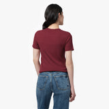 A female model with long, wavy black hair is shown from the back, standing against a plain white background. She is wearing a fitted, short-sleeved, burgundy T-shirt with a classic round neckline. The back of the T-shirt is plain with no visible branding or embellishments. She pairs it with high-waisted, medium-wash blue jeans that have a straight-leg fit and visible back pockets with contrast stitching. Her posture is relaxed, with her arms resting naturally at her sides while she slightly turns her head t