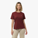Woman facing forward wearing a maroon t-shirt with small white embroidered dog logo on left chest and beige wide-leg pants
