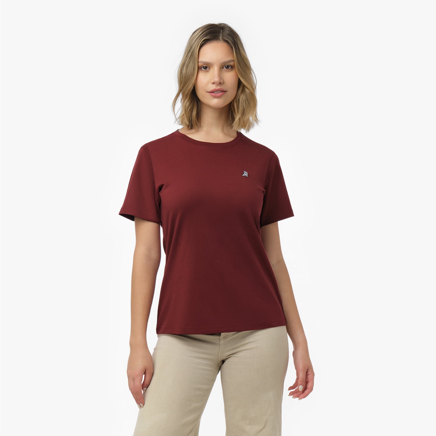 Woman facing forward wearing a maroon t-shirt with small white embroidered dog logo on left chest and beige wide-leg pants