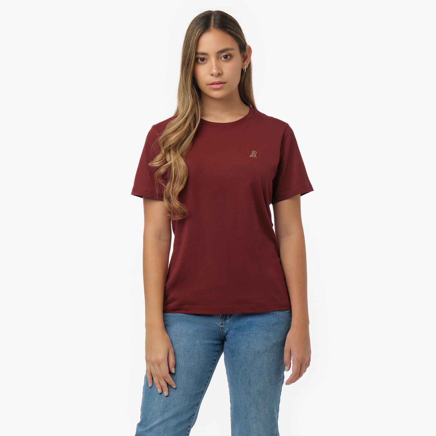 Woman facing forward wearing a maroon t-shirt with small gold embroidered dog logo on left chest and blue jeans