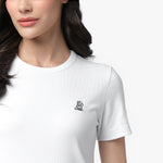 A close-up shot of a female model wearing a white, ribbed, short-sleeved T-shirt. The fabric has a fine ribbed texture, and the round neckline is neatly stitched. A small embroidered logo of a sitting dog, outlined in black, is visible on the left side of the chest. Part of the model’s