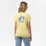 A woman is shown from behind, wearing a yellow T-shirt with a large circular graphic on the back. The design features a dog sitting in front of a tropical background with the text "James Bark Privé Society" around the circle. She pairs the shirt with light blue jeans.