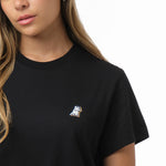 A close-up of the woman wearing the black T-shirt, focusing on the chest area with the small embroidered dog logo.