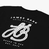 A close-up of the back design on the black T-shirt, showing the large white graphic with "James Bark Privé Society" and the rope initials "JB."