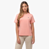 Woman facing forward wearing a peach-colored t-shirt with small white embroidered dog logo on left chest and beige wide-leg pants