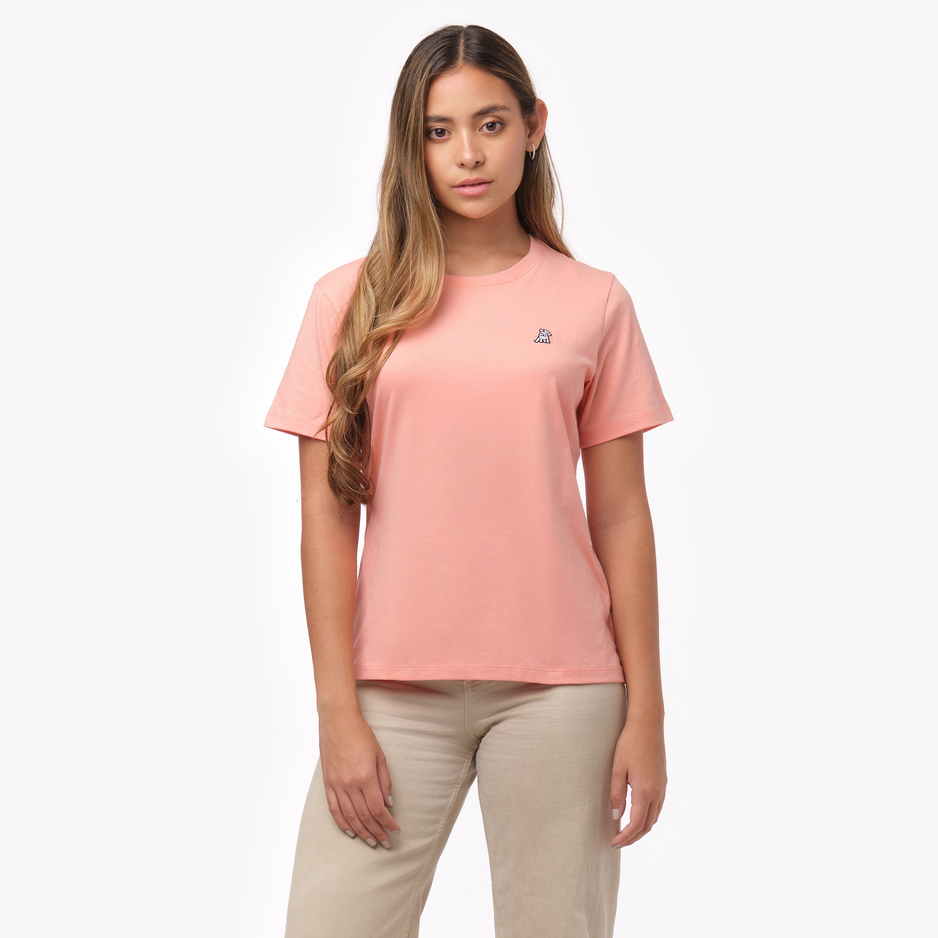 Woman facing forward wearing a peach-colored t-shirt with small white embroidered dog logo on left chest and beige wide-leg pants