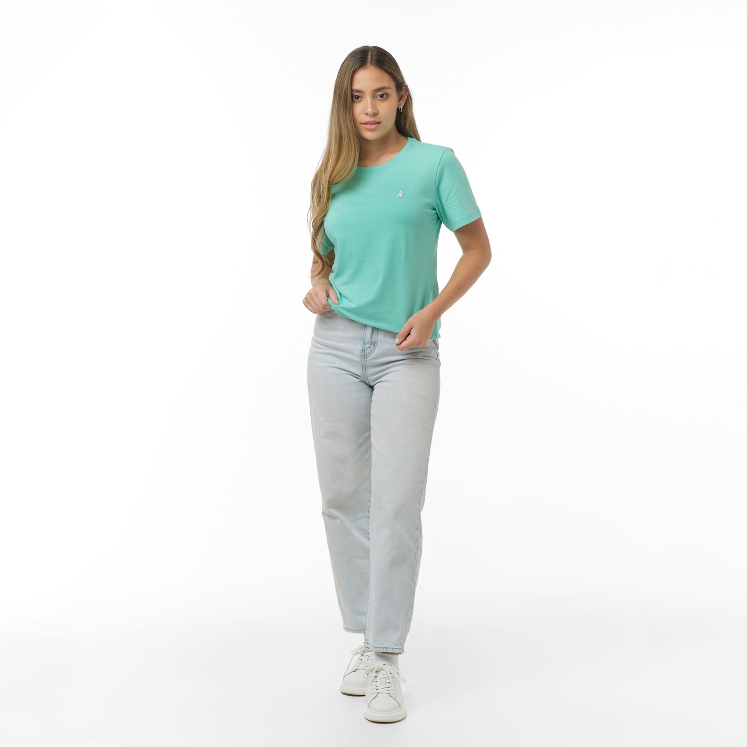 Woman facing forward wearing a mint green t-shirt with small white embroidered dog logo on left chest and light wash jeans