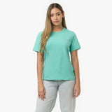 Woman walking forward, adjusting hem of mint green t-shirt with white logo, wearing light wash jeans and white sneakers