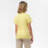 A woman is shown from behind, wearing the yellow T-shirt paired with beige pants. No design is visible on the back.