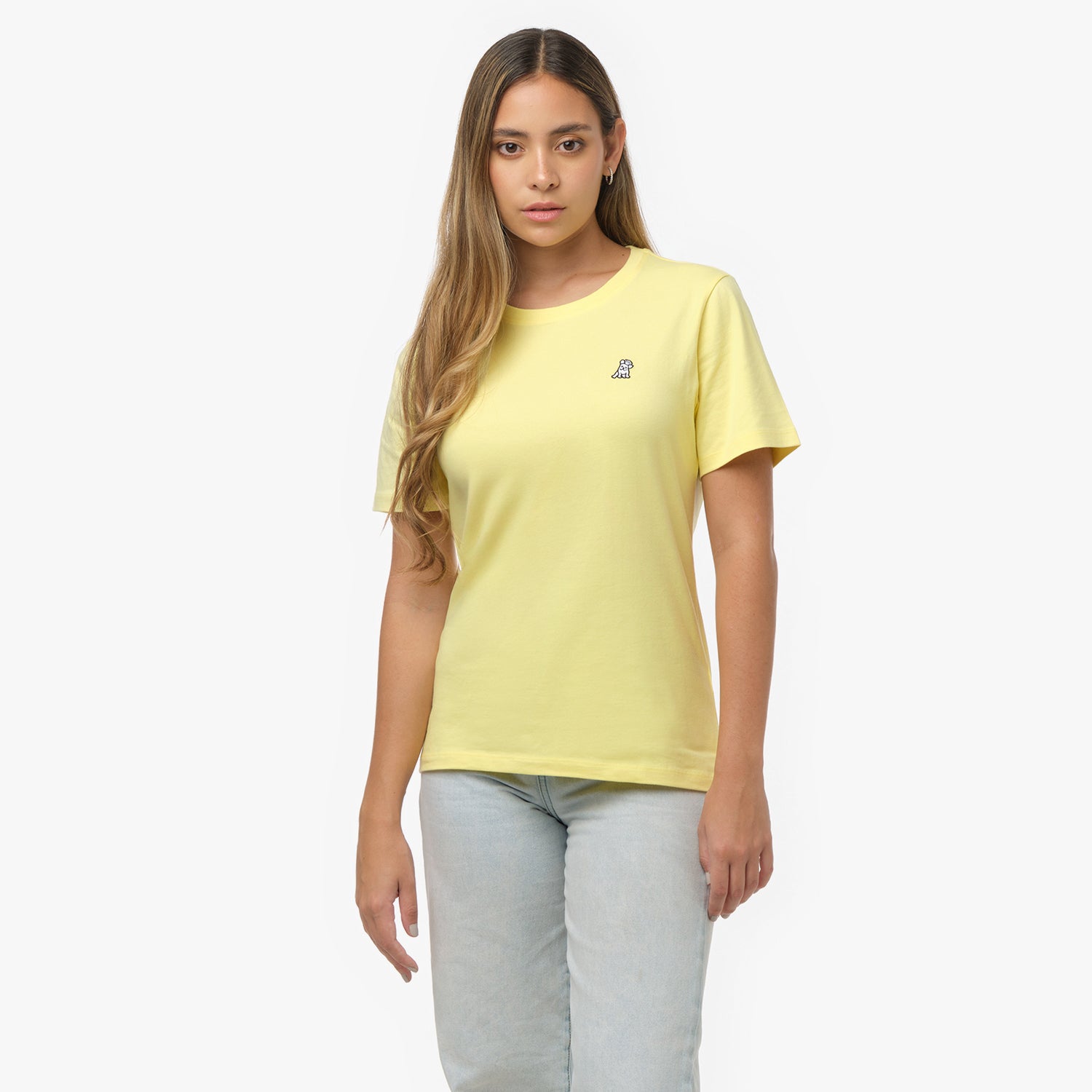 Woman facing forward wearing a pale yellow t-shirt with small white embroidered dog logo on left chest and light wash jeans