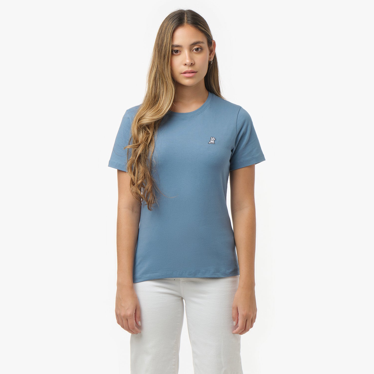 Woman facing forward wearing a dusty blue t-shirt with small white embroidered dog logo on left chest and white wide-leg pants