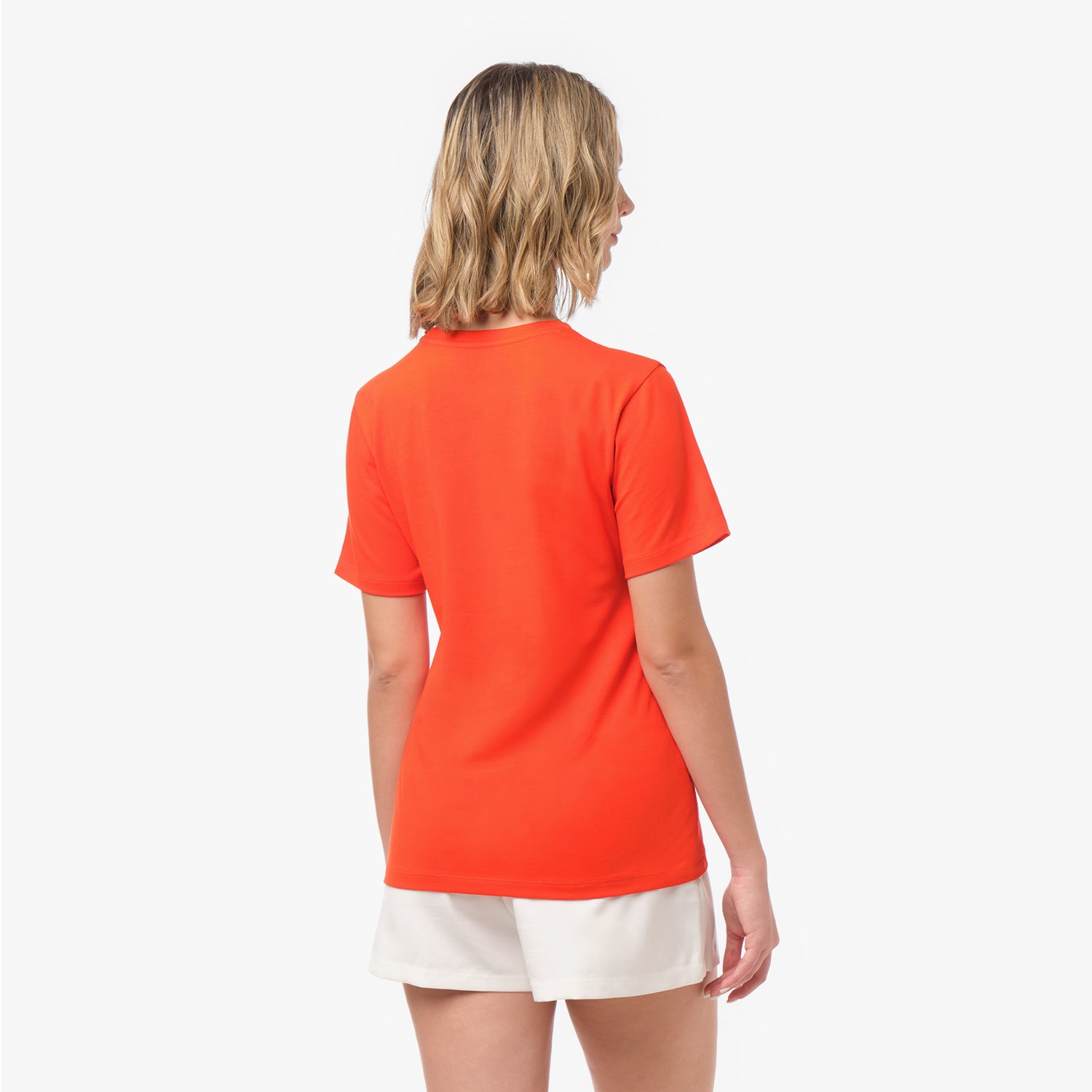 Back view of a woman wearing a plain bright orange t-shirt and white shorts