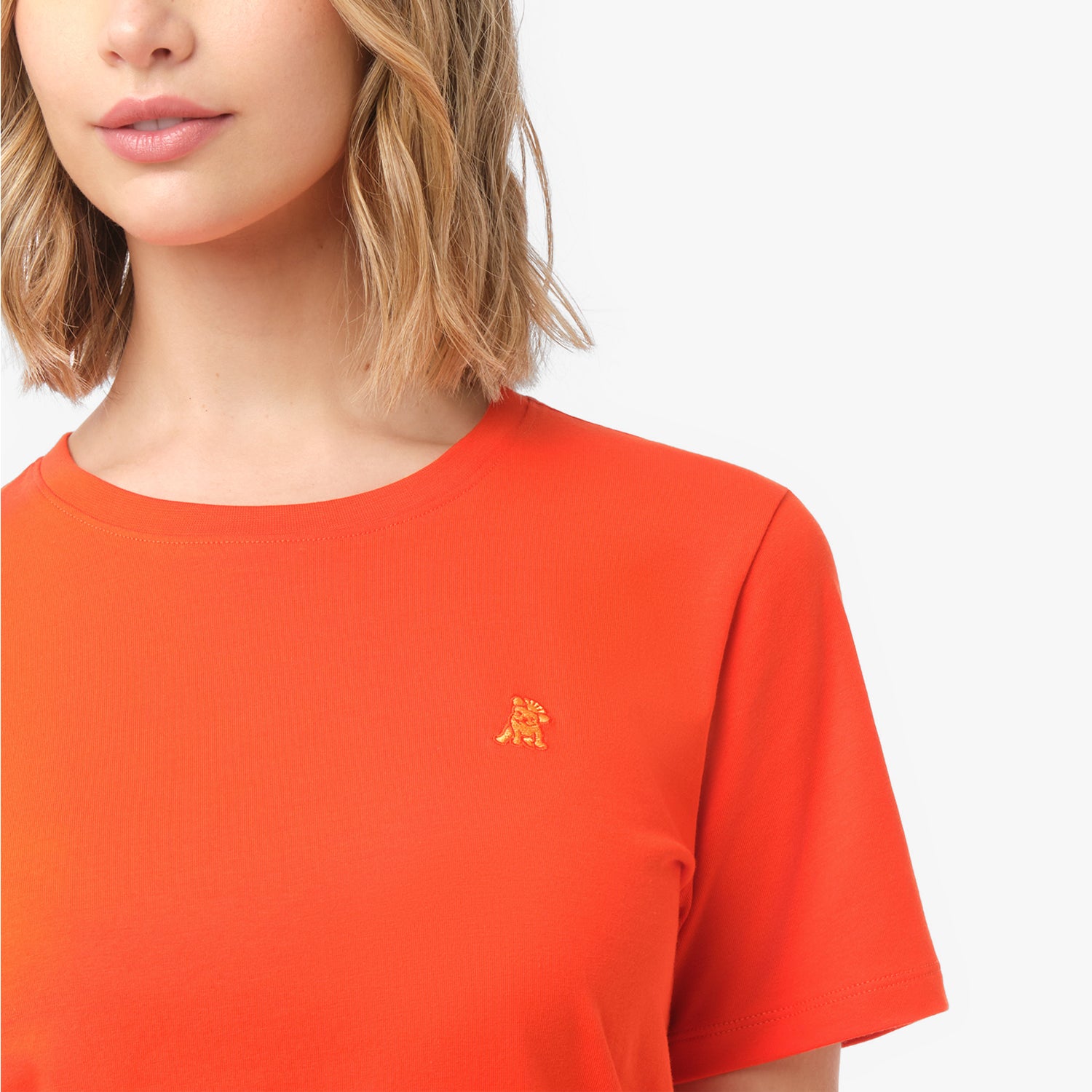 Close-up of the small, tone-on-tone embroidered dog logo on the left chest of the bright orange t-shirt