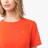 Close-up of the small, tone-on-tone embroidered dog logo on the left chest of the bright orange t-shirt