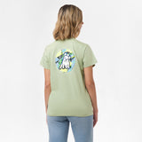 A woman is shown from behind, wearing a light green T-shirt with a large circular graphic on the back. The design features a dog sitting in front of a tropical background with the text "James Bark Privé Society" around the circle. She pairs the shirt with light blue jeans.