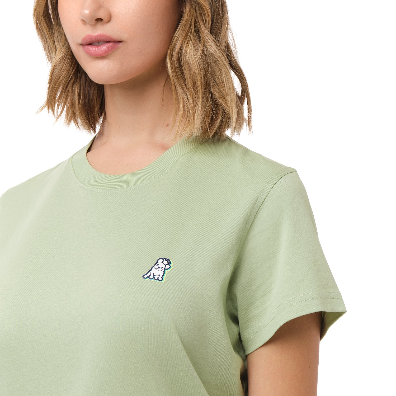 A close-up of the woman wearing the light green T-shirt, focusing on the chest area with the small embroidered dog logo.