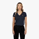 Front waist-up view of a female model wearing a navy blue v-neck t-shirt with a small gold embroidered logo on the left chest, paired with black trousers