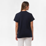 A woman is shown from behind, wearing the navy blue T-shirt paired with white pants. No design is visible on the back.