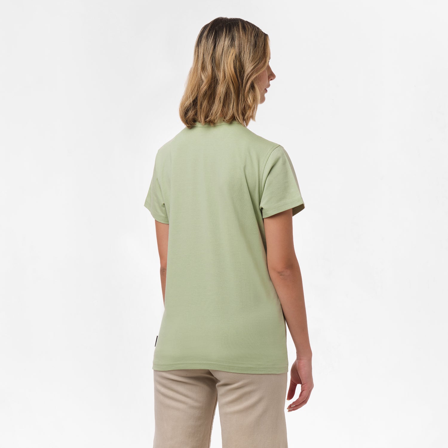 A woman is shown from behind, wearing the light green T-shirt paired with beige pants. No design is visible on the back.