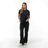 A full-body view of a woman wearing the navy blue T-shirt with the small embroidered dog logo on the chest, paired with black pants, standing with her hands in her pockets.