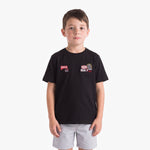 A young boy wearing a black T-shirt with two small racing-style chest patches and light gray shorts