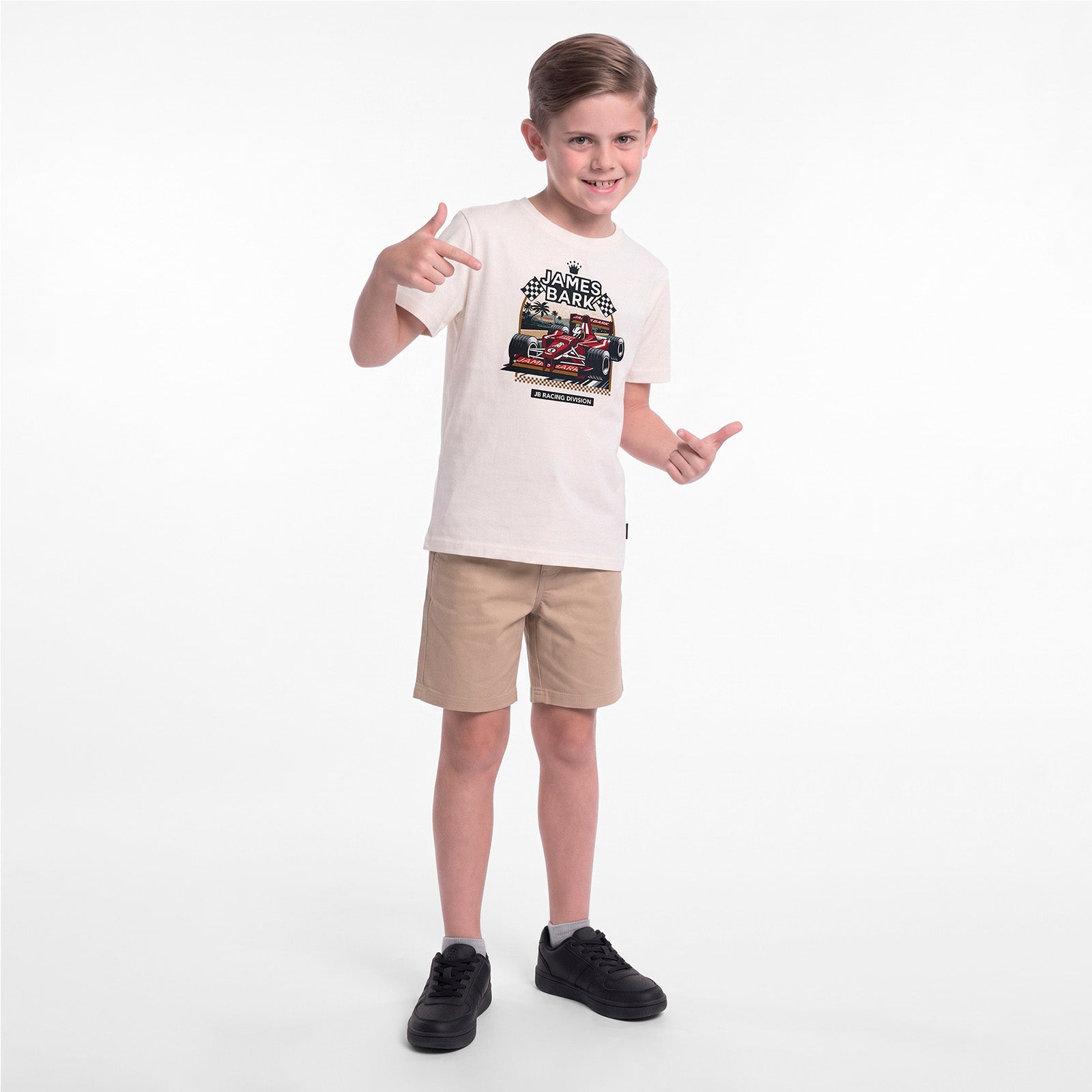 A young boy modeling a cream-colored graphic T-shirt, khaki shorts, and black sneakers