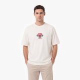 A man wearing a cream-colored crewneck t-shirt with a red and black 'James Bark Racing' chest graphic