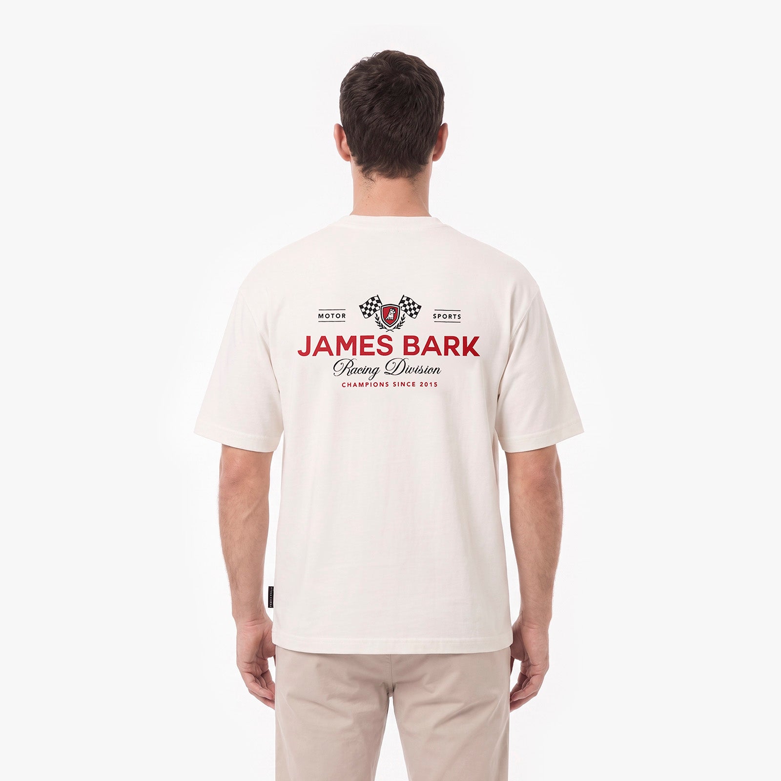 A man viewed from behind wearing a cream-colored T-shirt with a red and black James Bark Racing Division graphic on the back