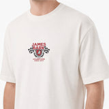 A close-up of a person wearing a white short-sleeve crewneck t-shirt with a red and black James Bark Champions graphic on the chest.