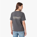 A woman shown from the back wearing a dark gray T-shirt with 'JAMES BARK ELEMENTS Structured Simplicity' printed in white on the back