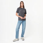 A woman modeling a dark gray short-sleeve T-shirt with small white text on the chest, paired with light blue jeans and white sneakers