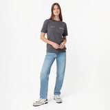 A woman modeling a dark gray short-sleeve T-shirt with small white text on the chest, paired with light blue jeans and white sneakers