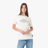 A woman modeling a cream-colored short-sleeve t-shirt with 'JAMES BANK ELEMENTS' printed in black on the chest