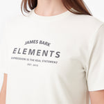 A close-up of a person wearing a cream-colored short-sleeve t-shirt with 'JAMES BARK ELEMENTS' printed in dark gray on the chest.