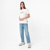 A woman modeling a white short-sleeve graphic T-shirt with 'ELEMENTS' printed on the chest, paired with light blue jeans and white sneakers