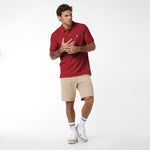 Man wearing a red polo shirt and beige shorts on a white background