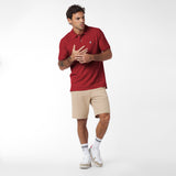 Man wearing a red polo shirt and beige shorts on a white background