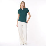 Full body picture of a woman wearing a green polo shirt and white pants on a white background