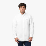 Full front view of a man wearing a white long-sleeved button-down shirt with a black and white logo and navy blue pants, standing against a white background