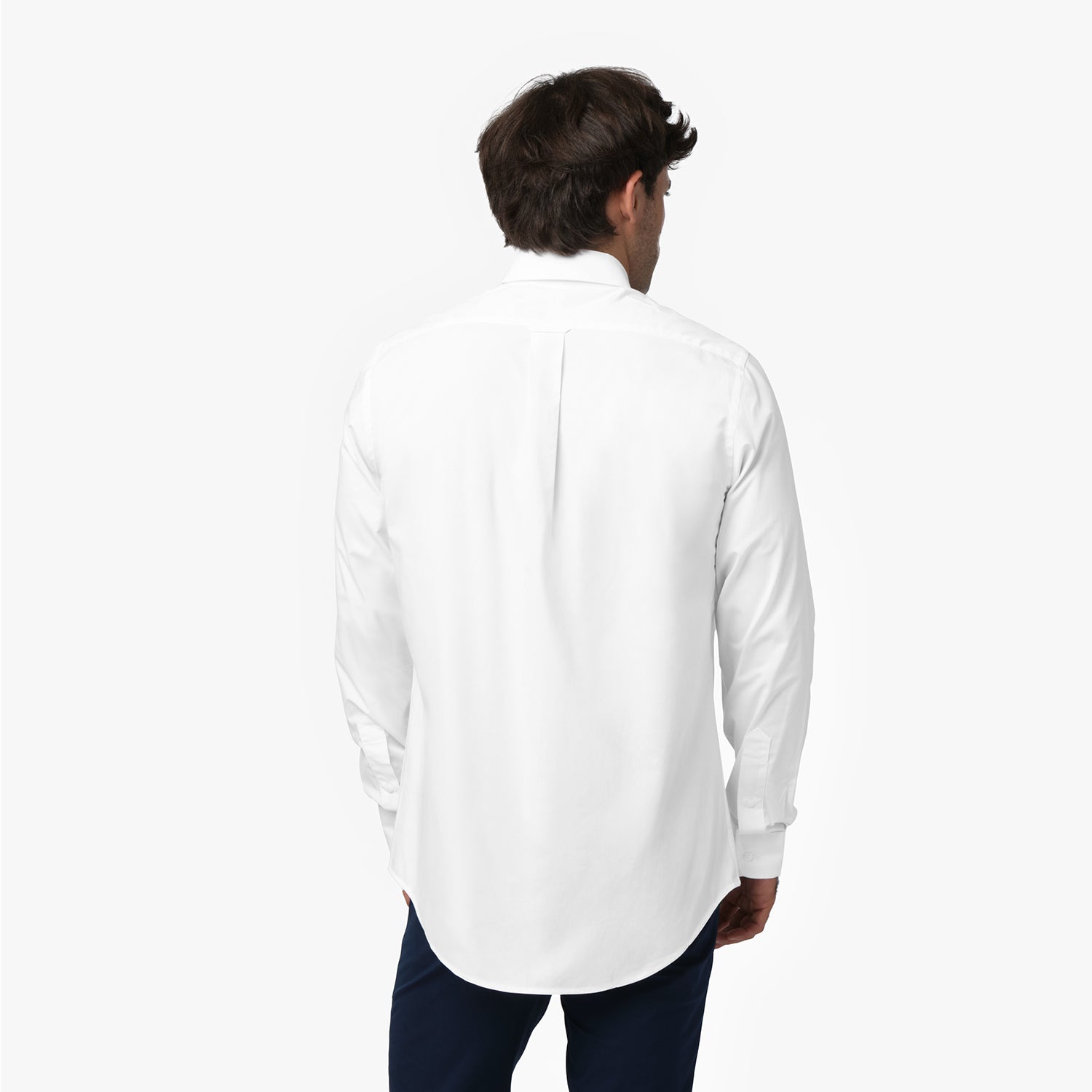 Back view of a man wearing a white long-sleeved shirt and navy blue pants against a white background, showing a box pleat on the back