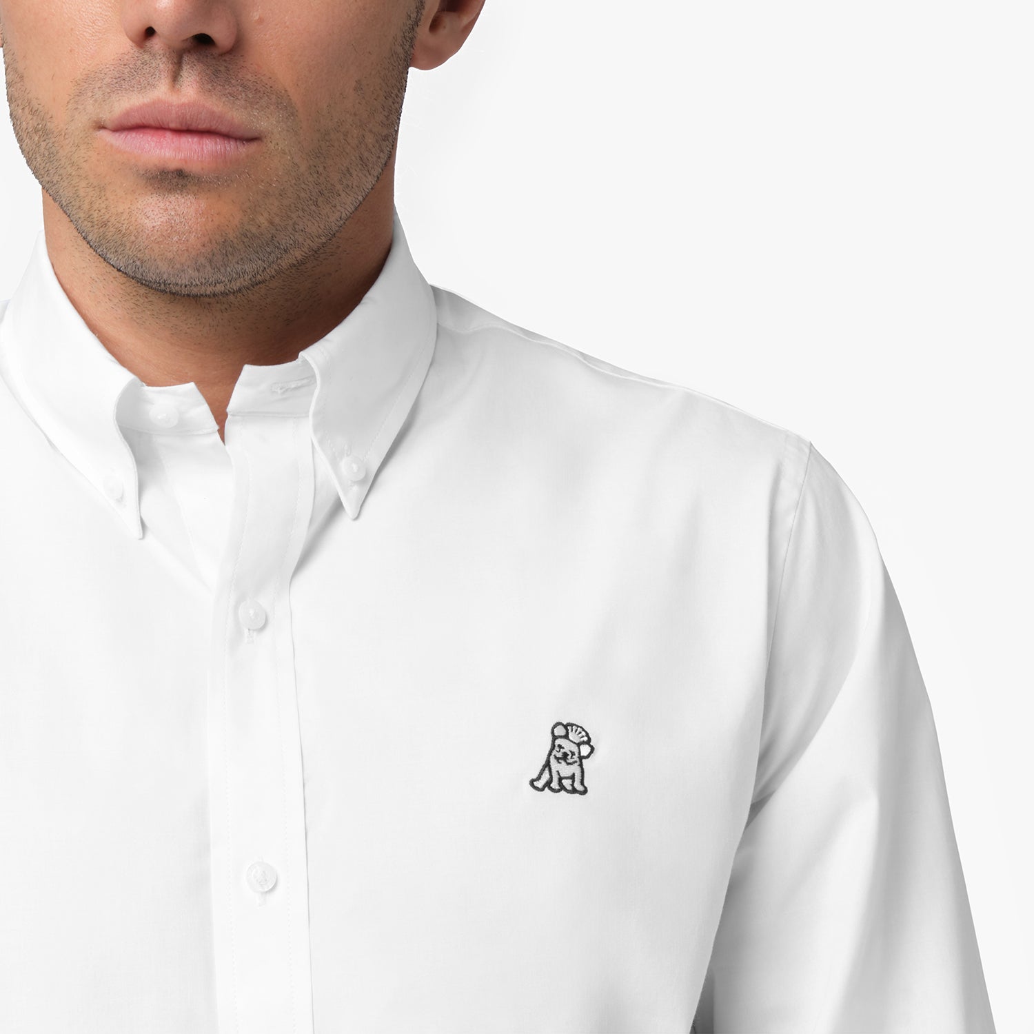 Close-up of a man wearing a white long-sleeved button-down shirt, showing the collar, white buttons, and the embroidered logo on the chest