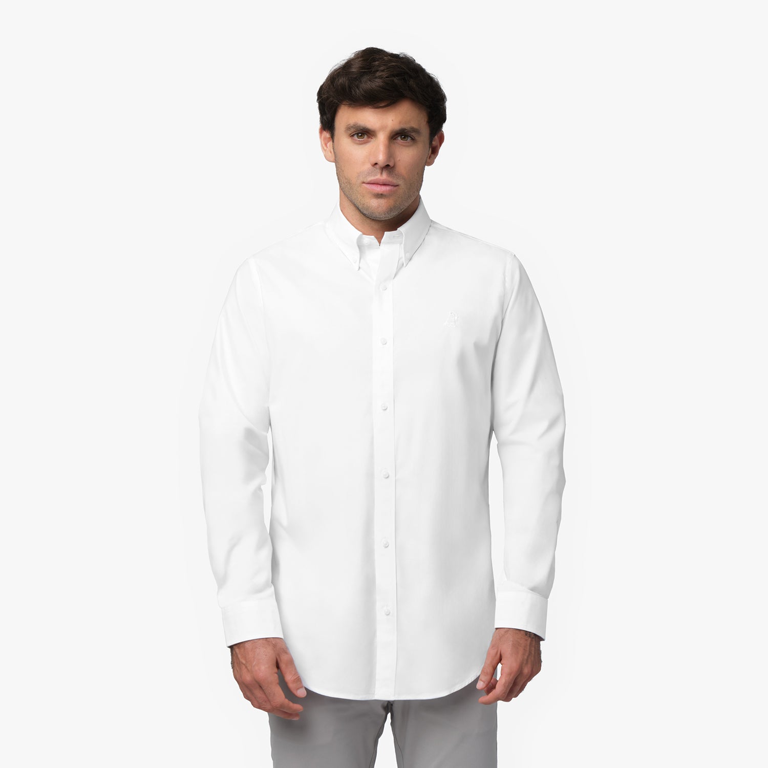 Full front view of a man wearing a white long-sleeved button-down shirt with a white logo and light grey pants, standing against a white background